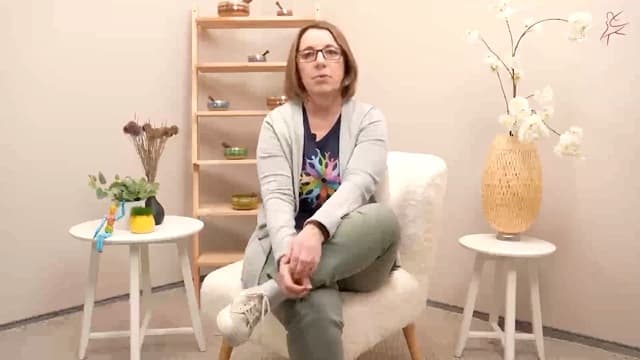 Eine Frau mit Brille sitzt entspannt in einem Sessel neben Pflanzen und Klangschalen