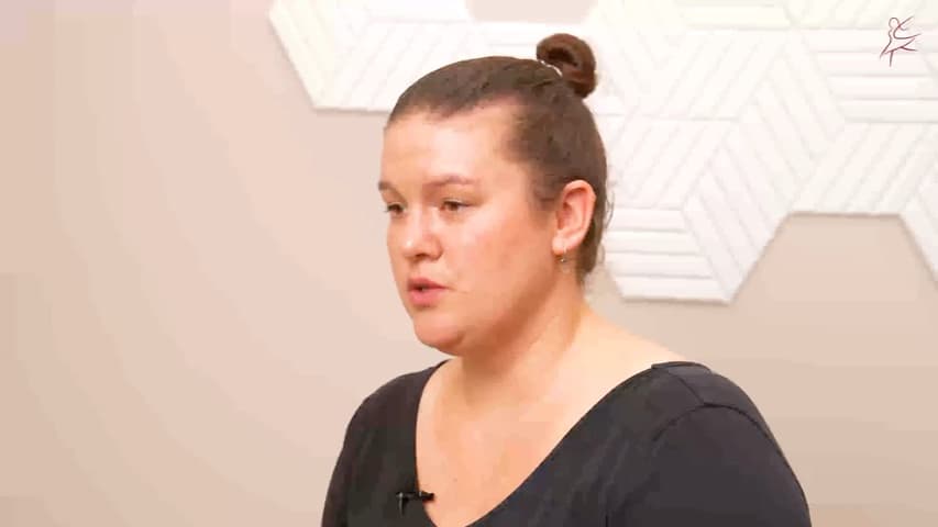 Eine Frau mit Haarknoten spricht im Interview vor einer hellen Wand
